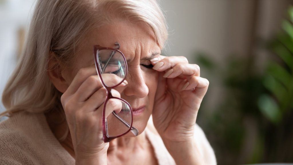 Ældre kvinde med briller i hånden gnider sig i øjnene.