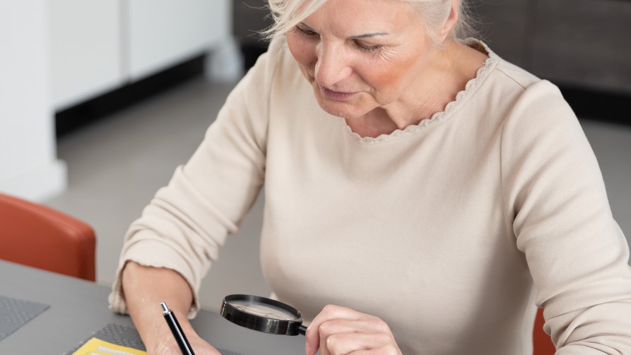 Ældre kvinde bruger lup til at se det hun skriver
