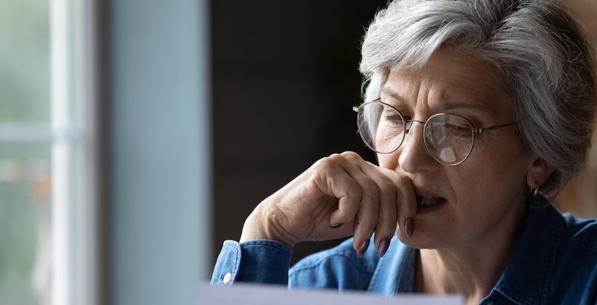 Senior kvinder med briller ser på dokument og ser eftertænksom ud