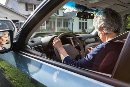 Ældre kvinde sidder bag rattet i bil og kigger undersøgende på instrumentbrættet