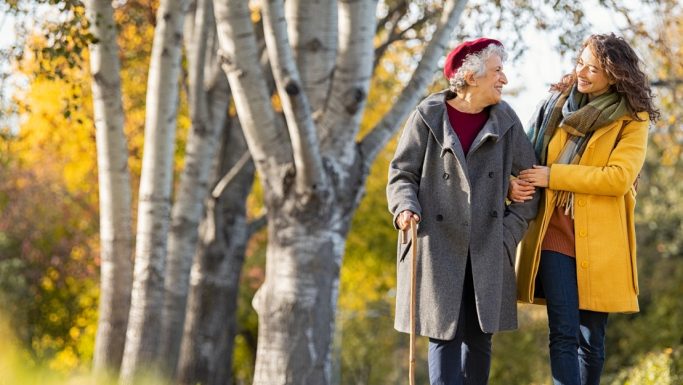 Senior kvinde går tur i efterårsskov ledsaget af ung kvinde