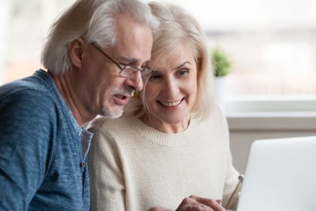 Senior mand med briller kigger på Computer med smilende senior kvinde