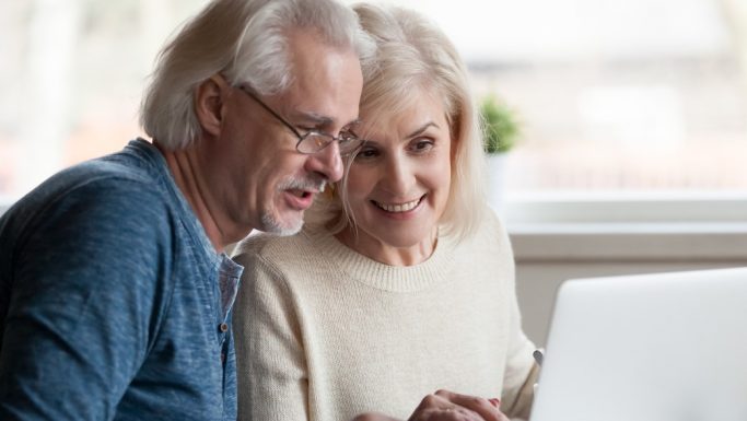 Senior mand med briller kigger på Computer med smilende senior kvinde