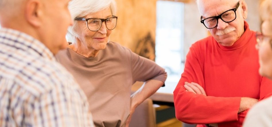 Senior mand og kvinde med briller står i rundkreds med to andre seniorer og taler