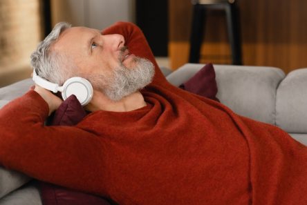 Senior mand ligger i sofa og lytter med høretelefoner på