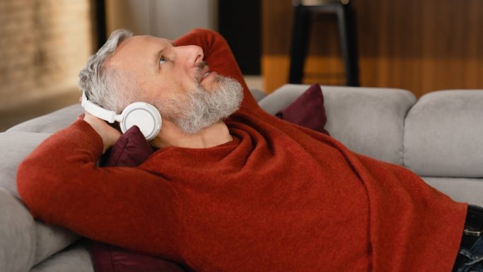 Senior mand ligger i sofa og lytter med høretelefoner på