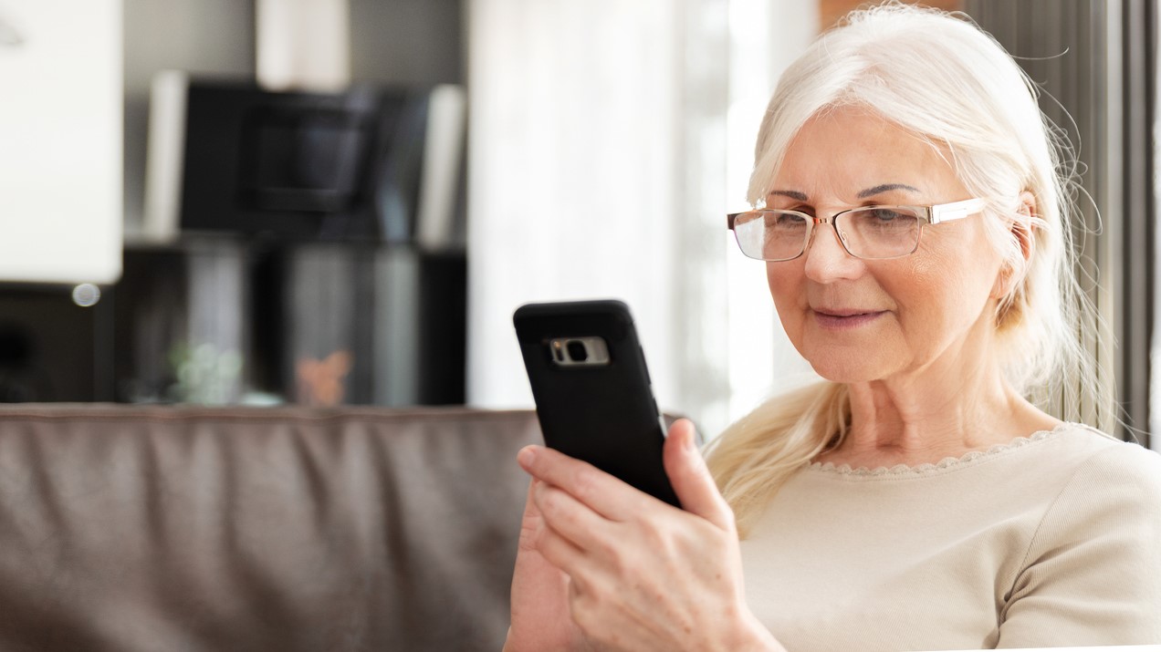 Senior kvinde med briller holder telefon ud for sig og smiler