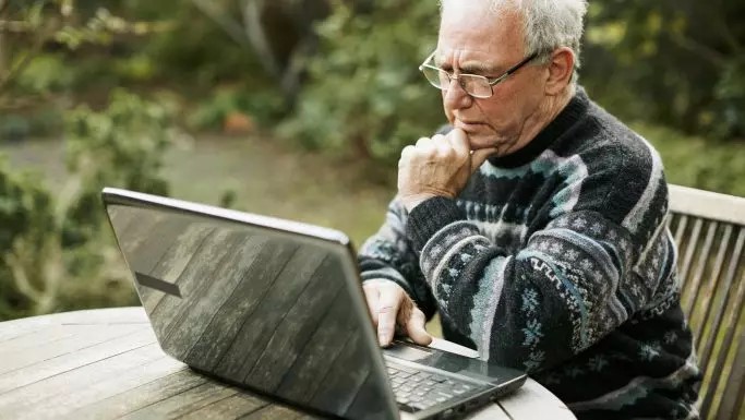 Senior mand med briller ser koncentreret på en bærbar computer