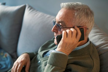 Senior mand med briller taler i telefon siddende i sofa