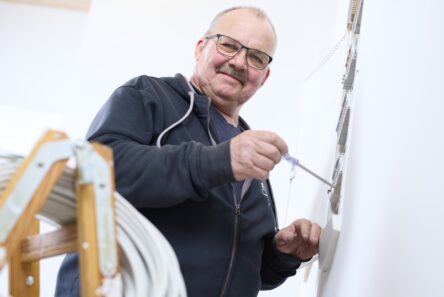 Senior mand med briller kigger smilende ned, mens han skruer på væg