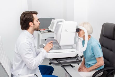 Senior kvinde kigger ind i stort måleapparat hos øjenlægen
