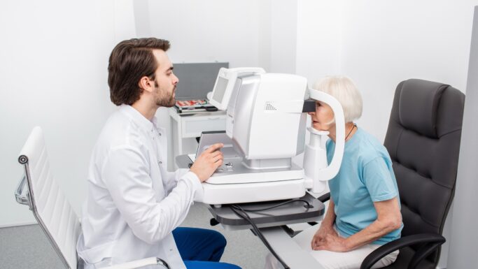 Senior kvinde kigger ind i stort måleapparat hos øjenlægen