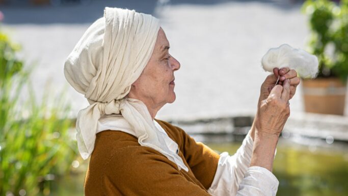 Catharina set i profil i middelaldertøj holder nysopundet garn op foran sig.